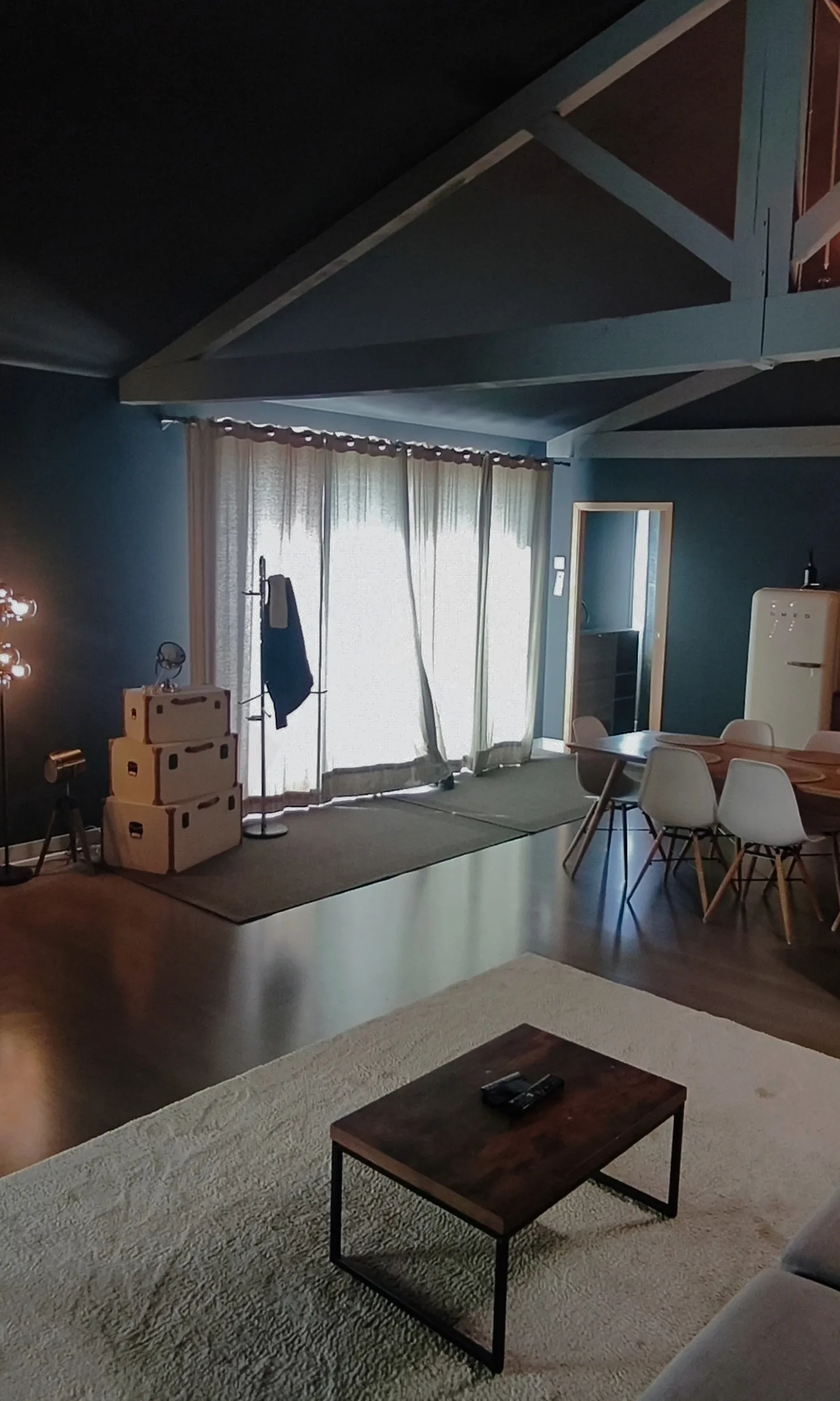 Le salon : télévision, charpente peinte, cuisine au fond, fauteuil jaune