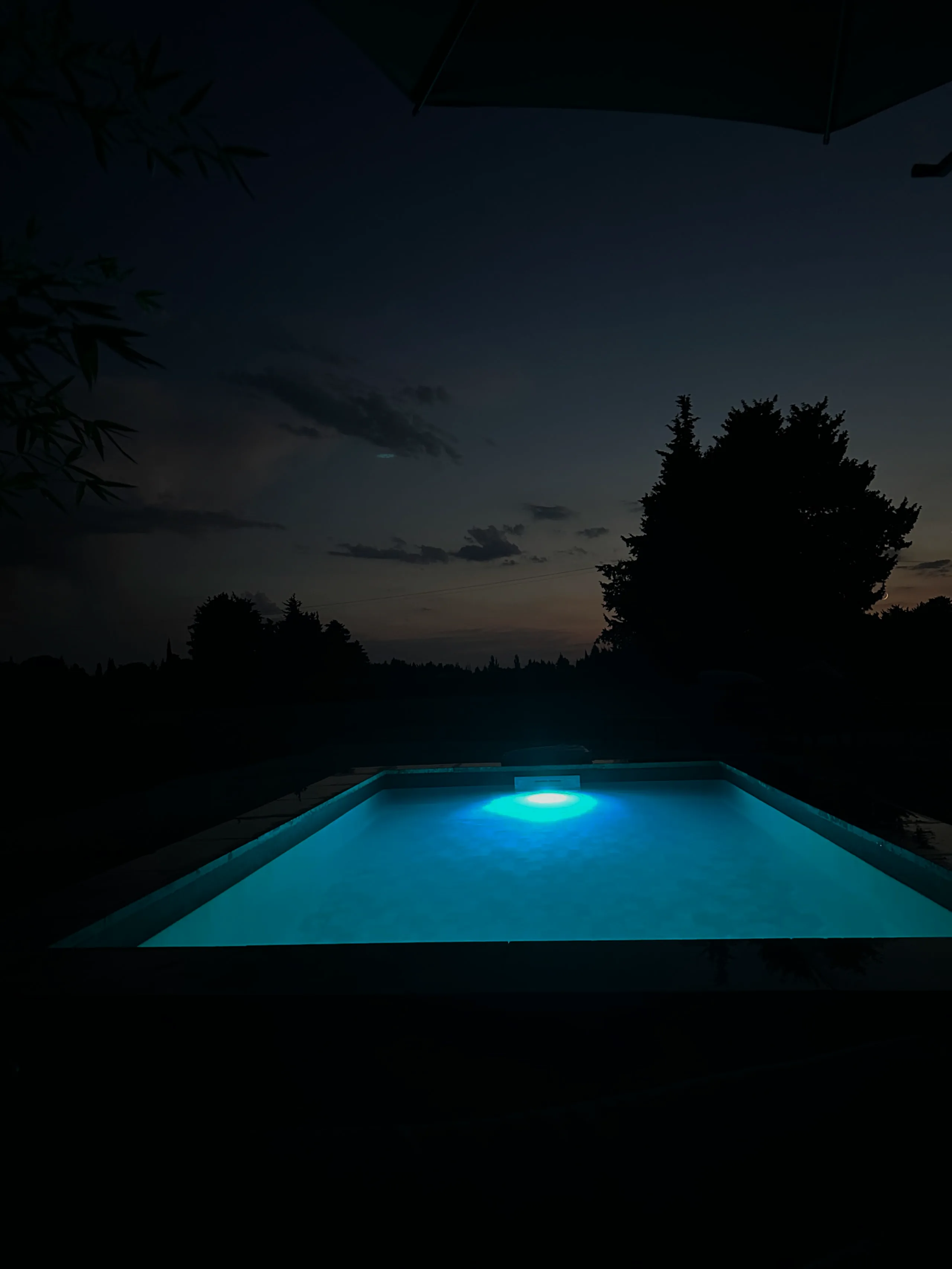La piscine éclairée à la tombée de la nuit, cyprès en silhouette