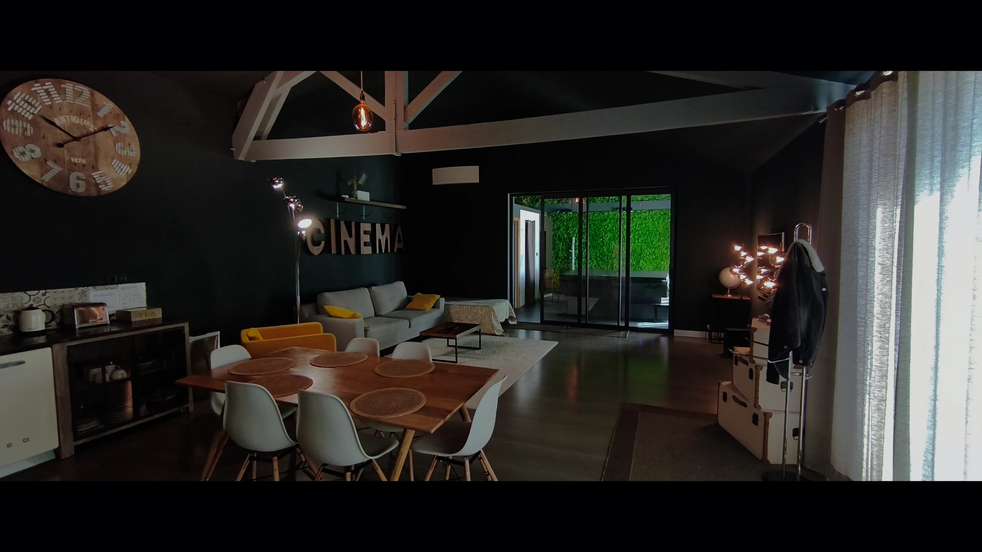 Le séjour en plan large : table, canapé, lettres CINEMA, baie sur le mur végétal