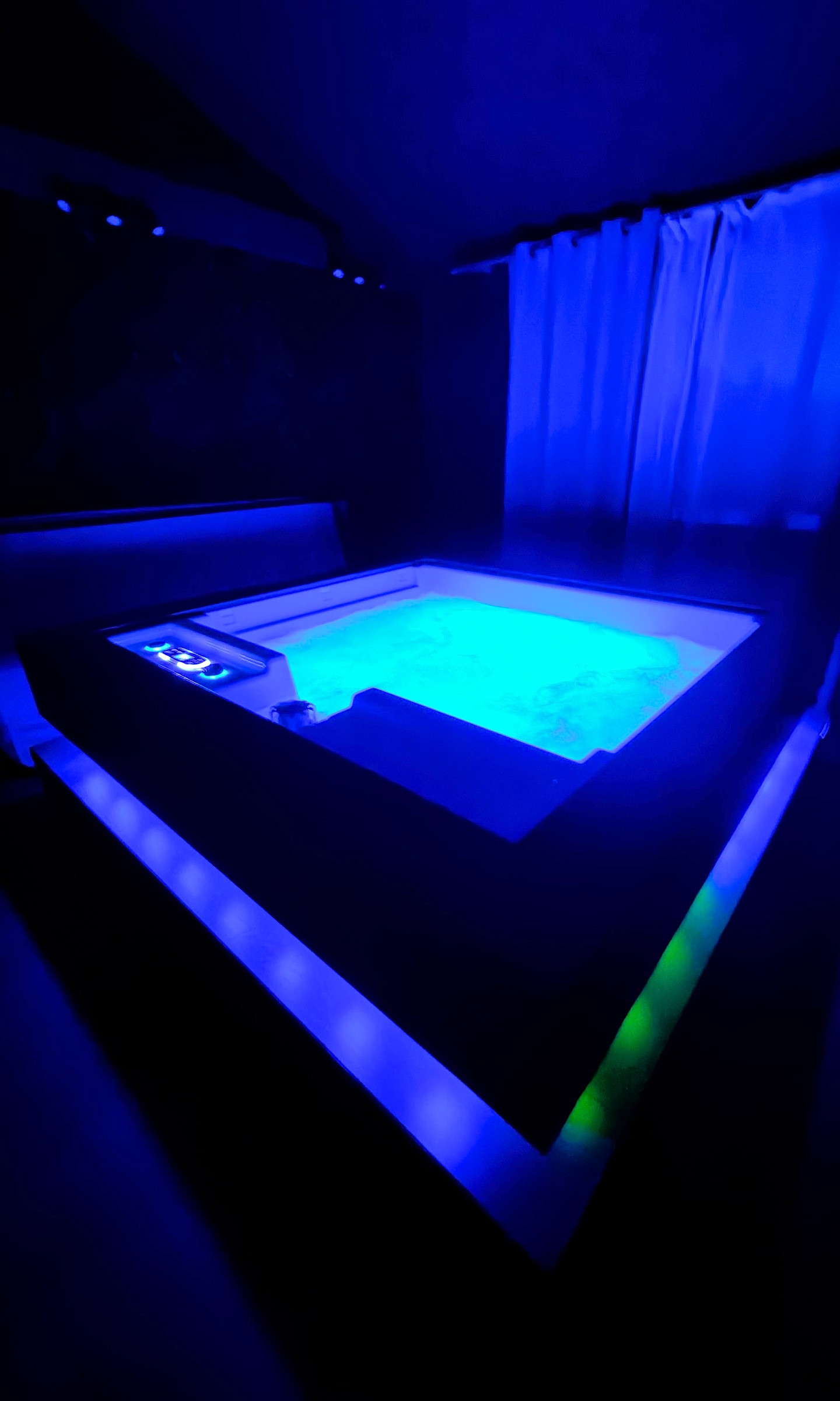 Le spa cube de nuit, eau turquoise et éclairage bleu, rideaux tirés